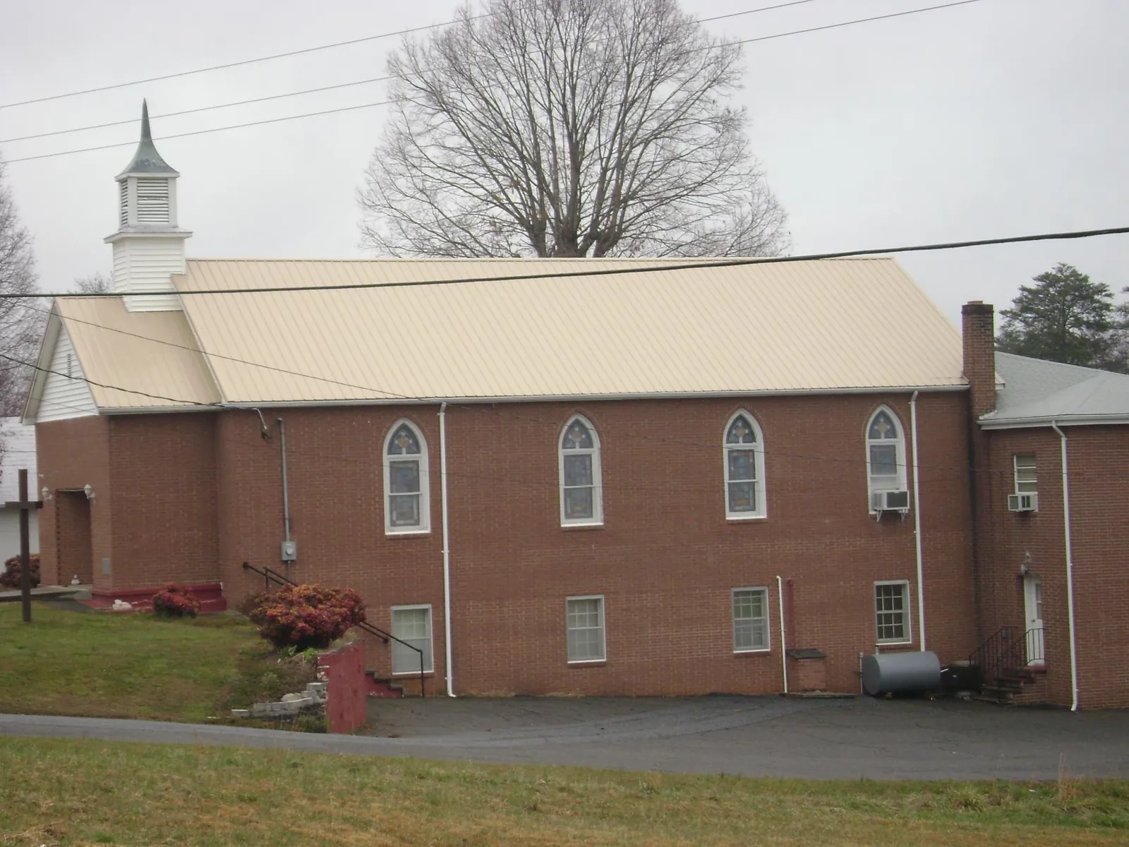 New tan metal roof on a brick church with a white steeple in Saint Marys